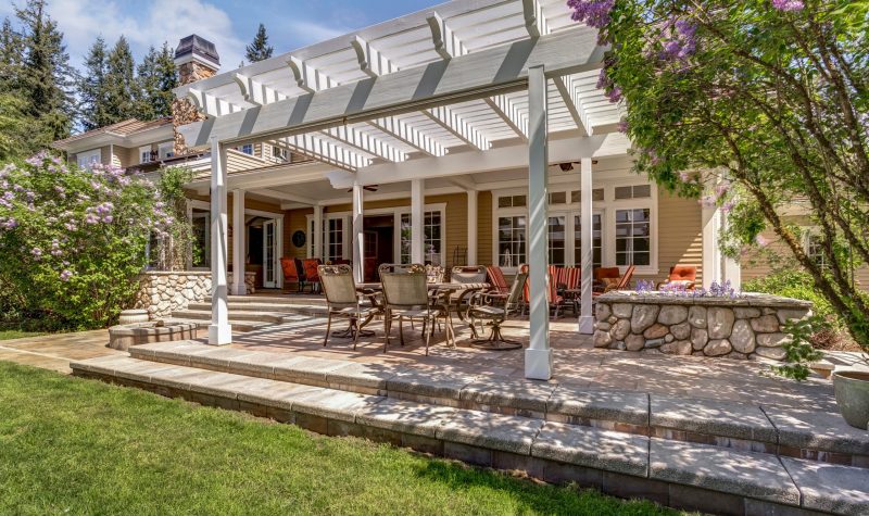 Lovely outdoor deck patio space with white dining pergola in the backyard of a luxury house.